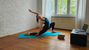 Frau auf Yogamatte macht Stretching vor einem Laptop