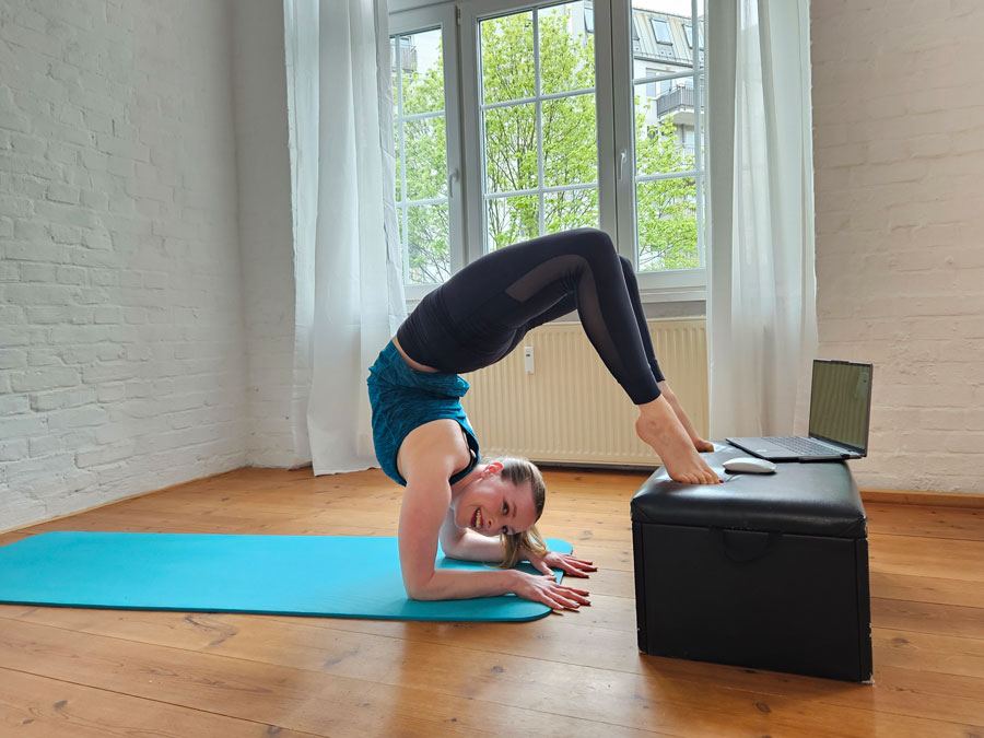 Eine Frau in Sportkleidung übt Unterarmstand auf einer Yogamatte vor einem Laptop