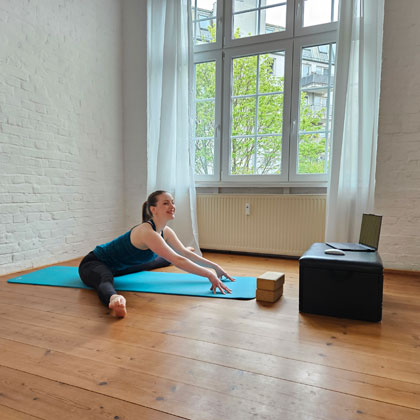 Eine Frau macht Stretching auf einer Yogamatte vor einem Laptop