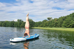Frau im Bikini macht Unterarmstand auf SUP in einem See