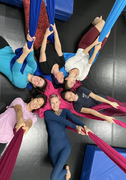 6 Frauen liegen in Sporthalle am Boden und greifen Aerial Silks